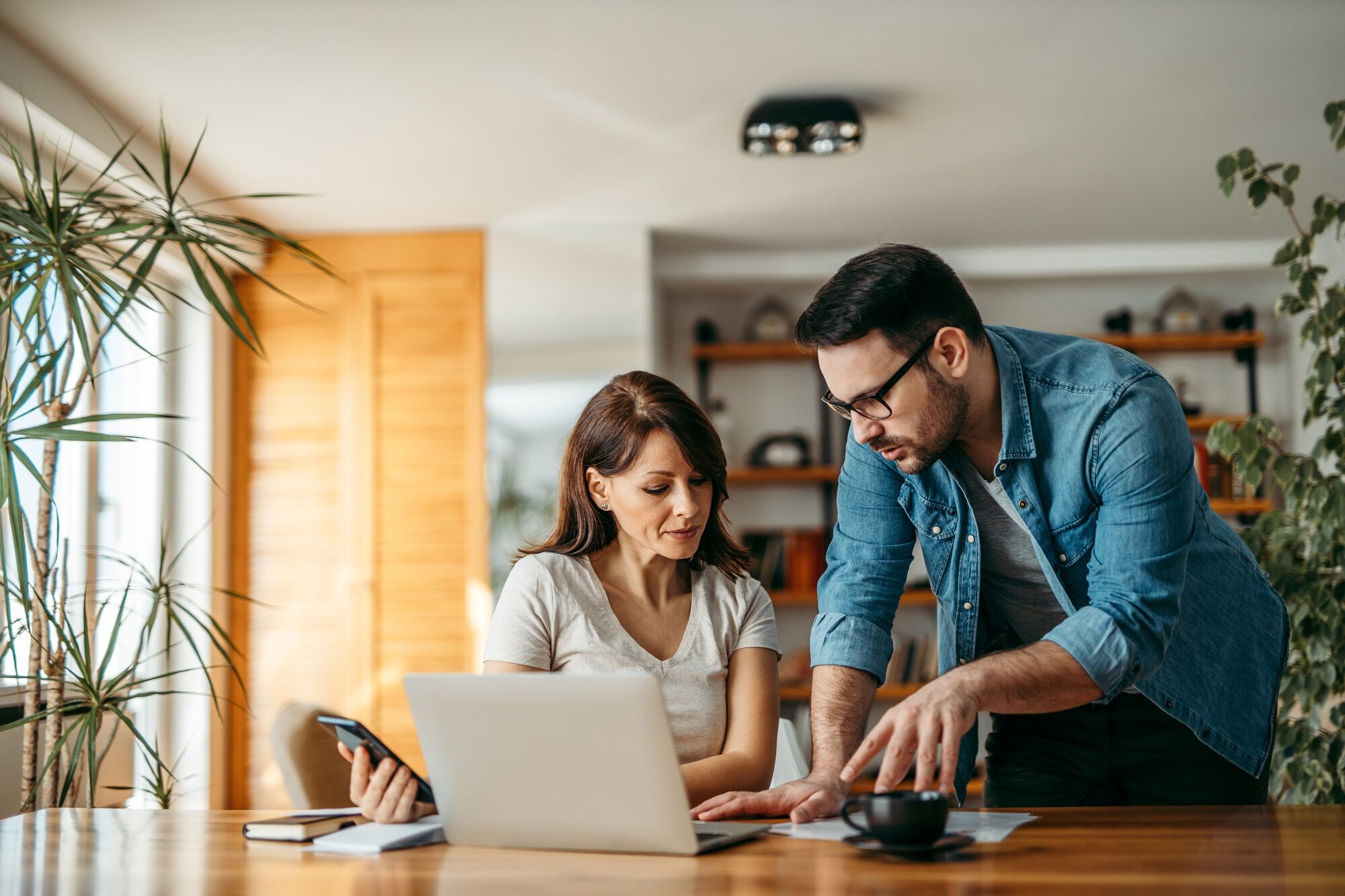 Two people discussing paperwork and working on a laptop, portrait.